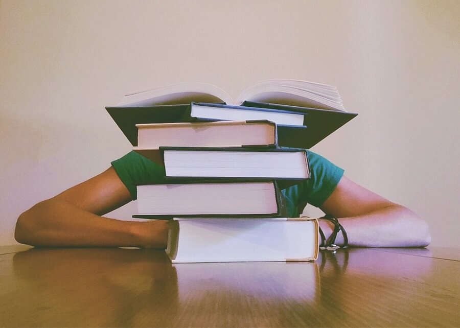 student with head on table behind stack of books