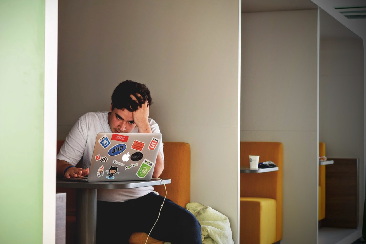 frustrated man wearing white t-shirt  and working on a macbook pro